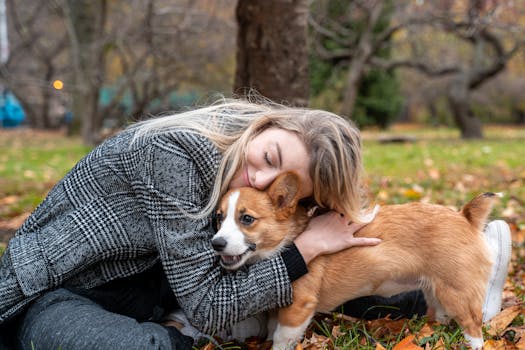 A woman cuddles her corgi puppy amidst fallen leaves in a New York City park.